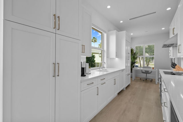 kitchen with light countertops, light wood-style floors, white cabinets, a sink, and extractor fan