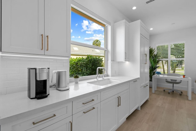 kitchen featuring tasteful backsplash, light countertops, white cabinetry, a sink, and light wood-type flooring