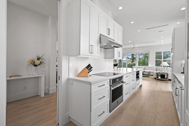 kitchen featuring black electric stovetop, light wood-style flooring, oven, under cabinet range hood, and open floor plan