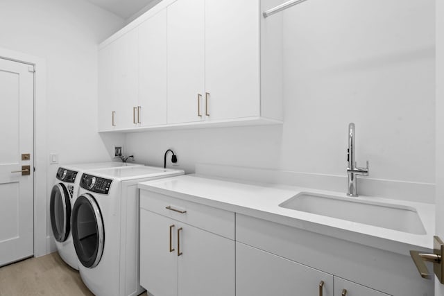 laundry area featuring independent washer and dryer, cabinet space, a sink, and light wood finished floors