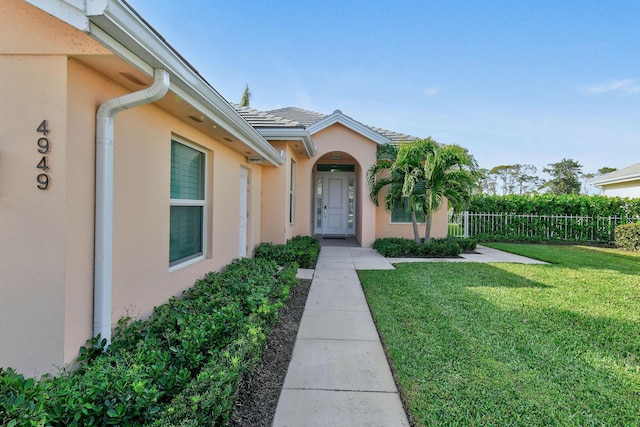 doorway to property with a tile roof, a lawn, fence, and stucco siding