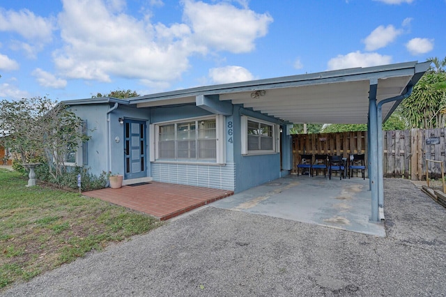 view of front of property featuring a carport, aphalt driveway, fence, and stucco siding