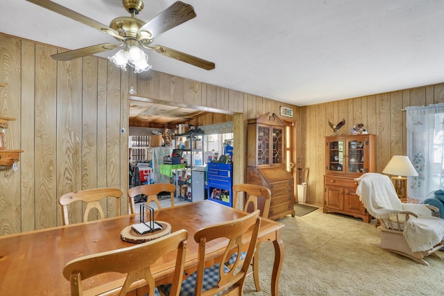 dining area featuring carpet floors, ceiling fan, and wooden walls