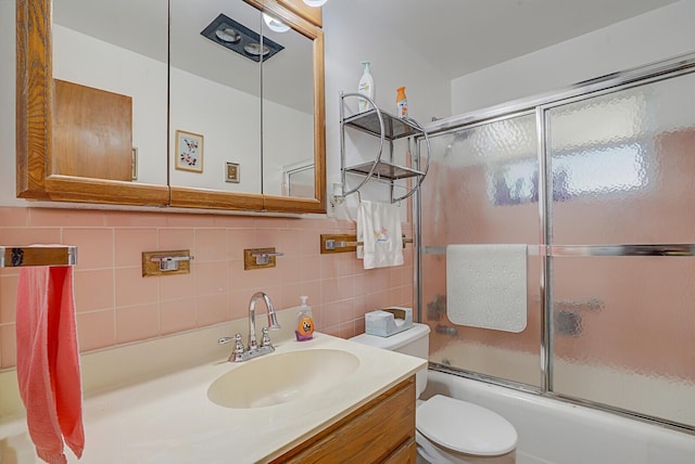 full bath featuring tile walls, shower / bath combination with glass door, vanity, and toilet