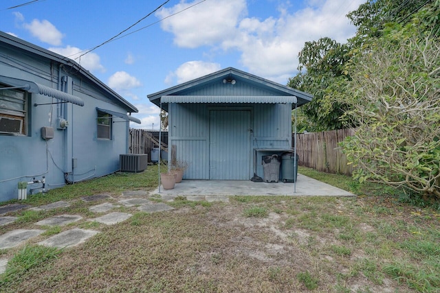 back of property featuring central AC unit, a fenced backyard, a storage unit, a yard, and an outdoor structure