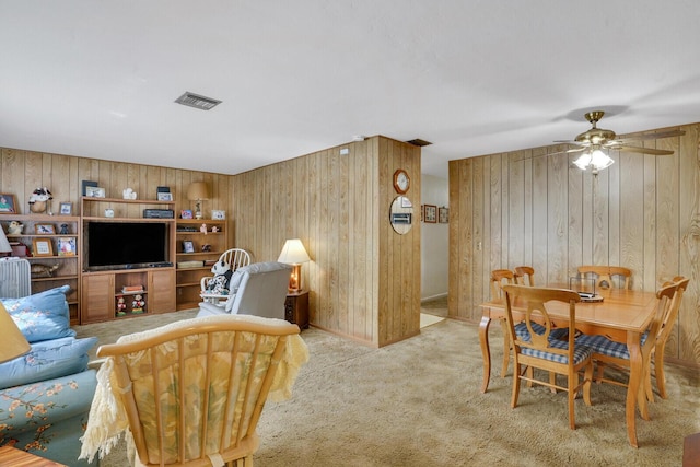 living area featuring carpet, wooden walls, visible vents, and ceiling fan