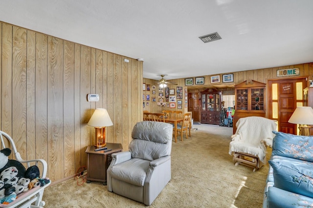 carpeted living area with ceiling fan, visible vents, and wooden walls