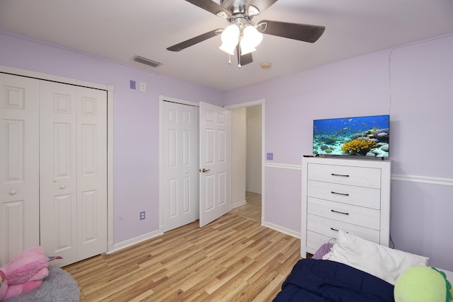 bedroom with visible vents, baseboards, a ceiling fan, light wood-style floors, and multiple closets