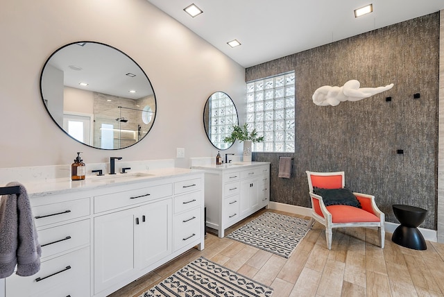 full bath with a sink, two vanities, wood finished floors, and a tile shower