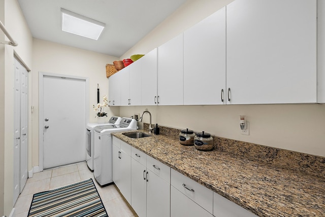 laundry room with a sink, cabinet space, a skylight, light tile patterned floors, and washing machine and clothes dryer