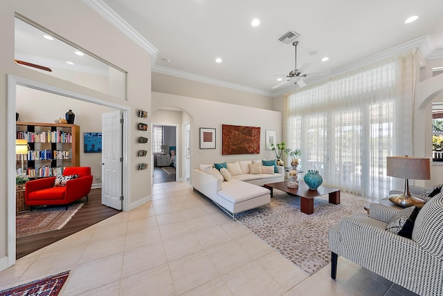 tiled living room with visible vents, arched walkways, ceiling fan, and crown molding