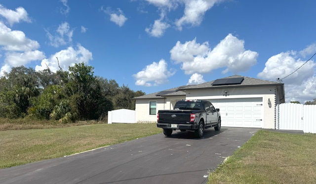 view of front of property featuring stucco siding, solar panels, an attached garage, fence, and a front lawn