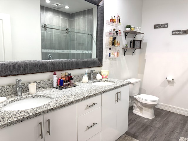 bathroom featuring double vanity, a sink, a shower stall, and wood finished floors