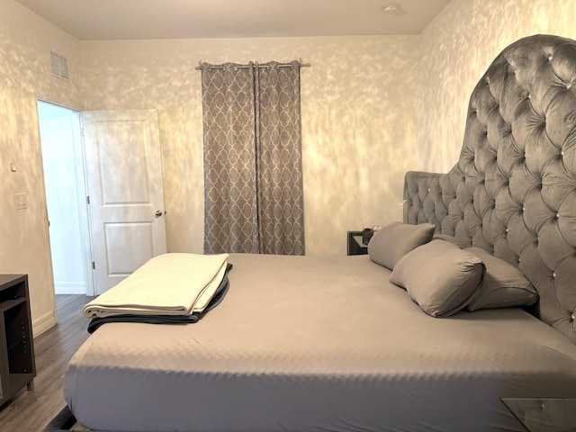 bedroom with visible vents, dark wood finished floors, baseboards, and wallpapered walls