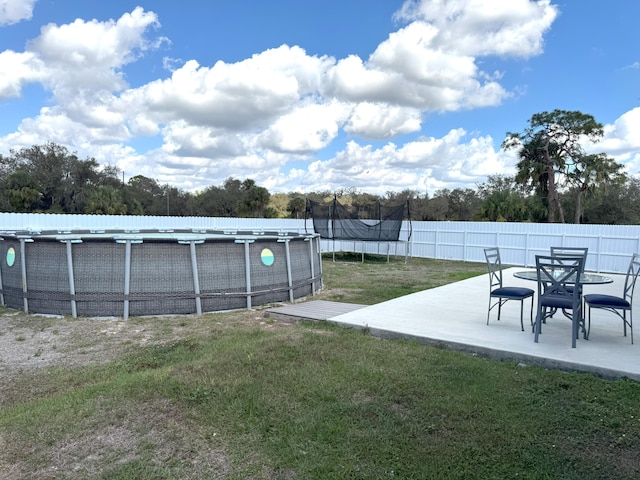 view of yard with a patio area, a trampoline, fence, and a fenced in pool