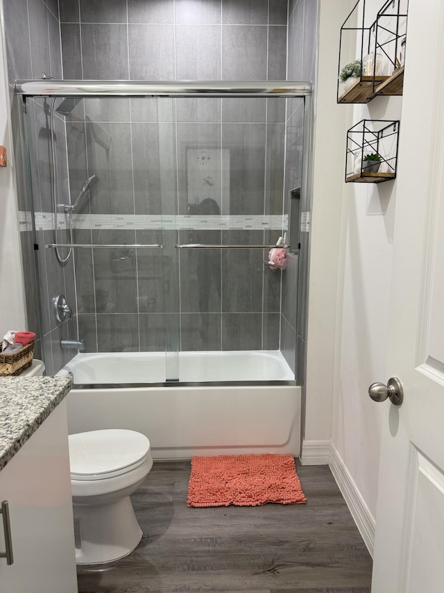 full bath with shower / bath combination with glass door, toilet, vanity, wood finished floors, and baseboards