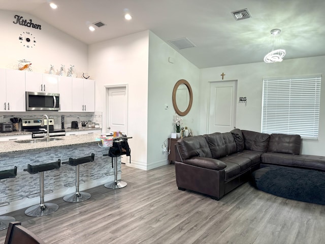 living room with high vaulted ceiling, light wood-type flooring, visible vents, and baseboards