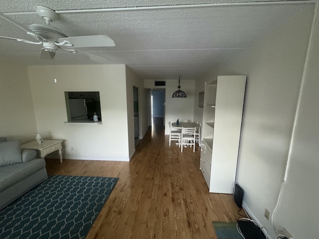 interior space with a ceiling fan, a textured ceiling, wood finished floors, and baseboards