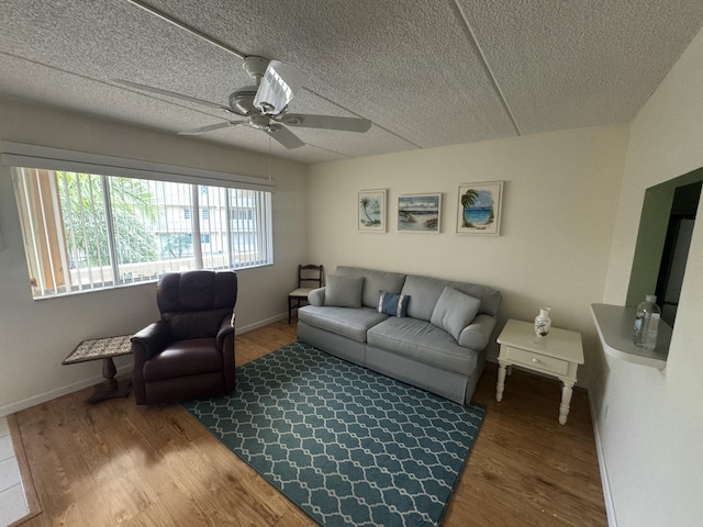 living room featuring baseboards, wood finished floors, ceiling fan, and a textured ceiling