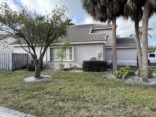 view of front of house with stucco siding, a tiled roof, fence, and a front yard