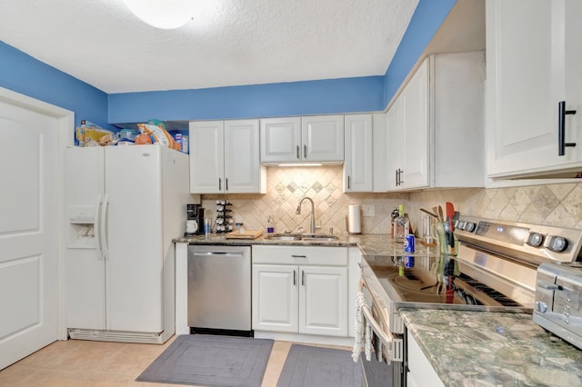 kitchen featuring light tile patterned floors, stainless steel appliances, stone counters, white cabinetry, and a sink