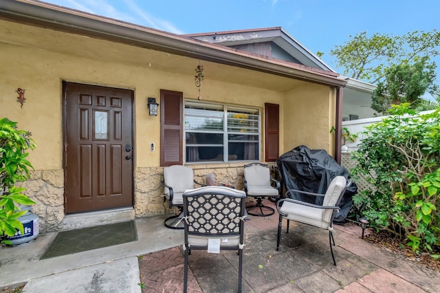 view of exterior entry featuring a patio area, stone siding, and stucco siding