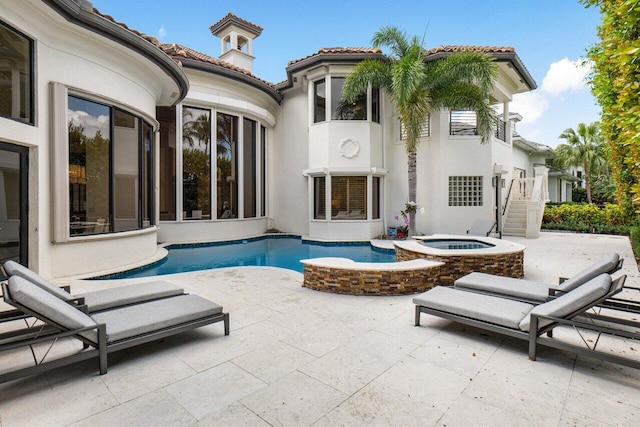 rear view of property featuring an in ground hot tub, a tiled roof, stucco siding, an outdoor pool, and a patio area