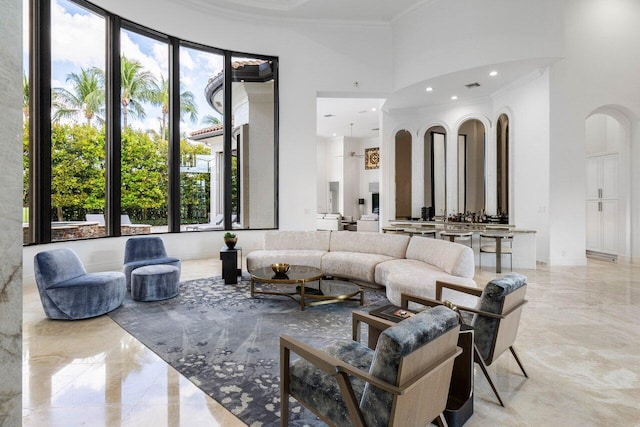 living area with arched walkways, marble finish floor, a high ceiling, and crown molding