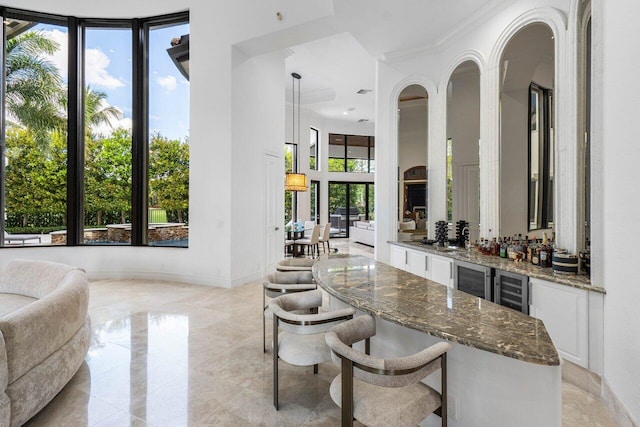 bar with beverage cooler, baseboards, a high ceiling, crown molding, and indoor wet bar