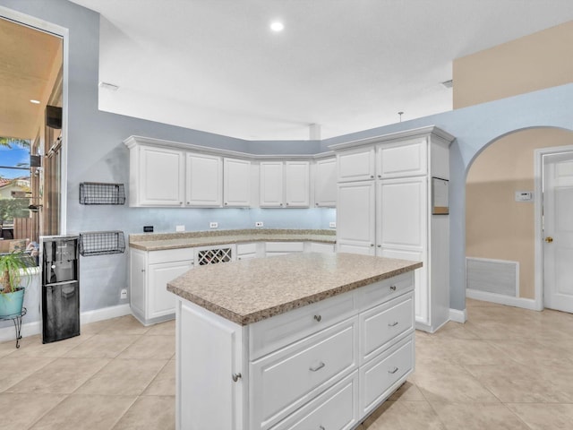 kitchen featuring visible vents, arched walkways, a kitchen island, light countertops, and white cabinetry