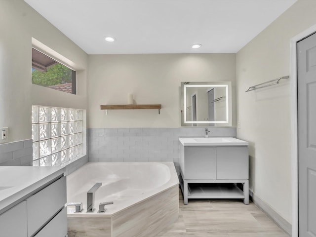 full bathroom featuring recessed lighting, two vanities, a garden tub, and a sink