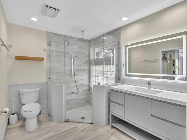 bathroom with toilet, vanity, visible vents, tile walls, and a stall shower