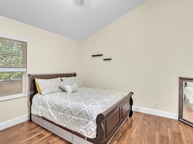 bedroom featuring vaulted ceiling, a textured ceiling, wood finished floors, and baseboards