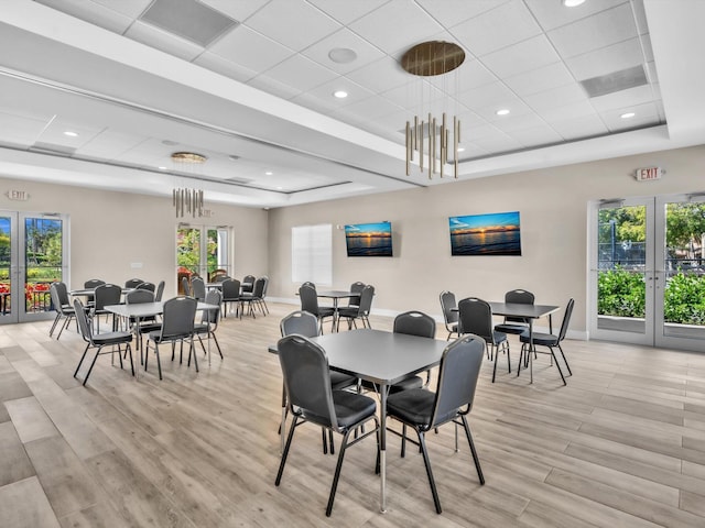 dining area with french doors, a raised ceiling, light wood-style flooring, and baseboards