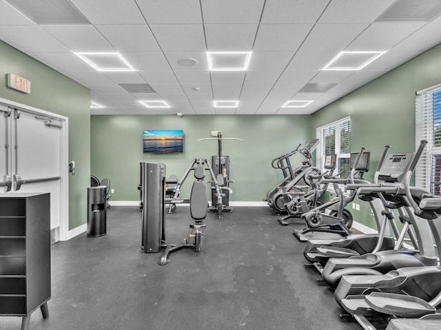 gym with a paneled ceiling and baseboards