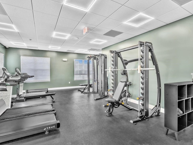 gym featuring a paneled ceiling and baseboards