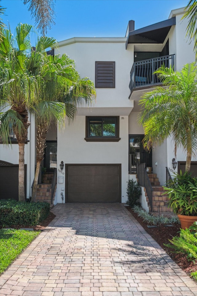 view of front of house with stucco siding, decorative driveway, a garage, and a balcony