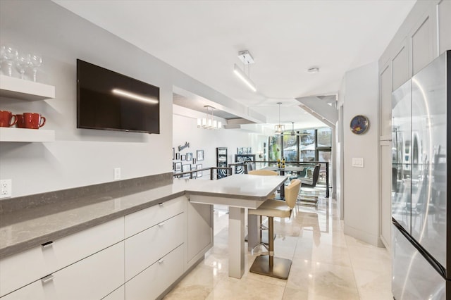 kitchen with pendant lighting, stainless steel fridge, an inviting chandelier, and white cabinetry