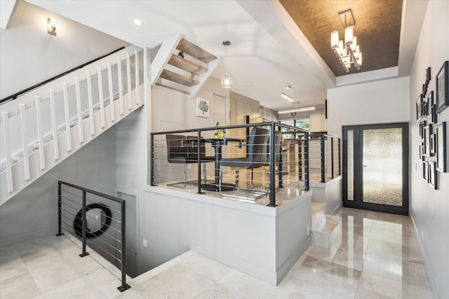 foyer with stairs, baseboards, a raised ceiling, and an inviting chandelier