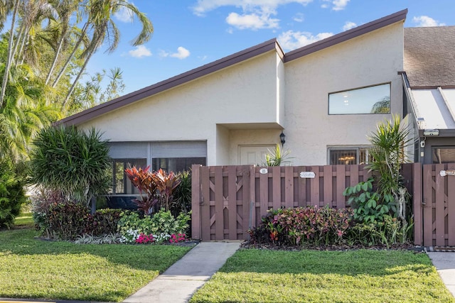 view of front of property with a front yard, a gate, fence, and stucco siding