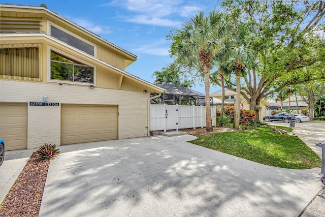 view of side of home featuring driveway, brick siding, an attached garage, and fence