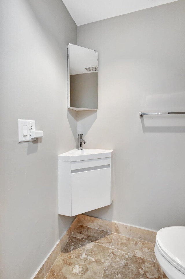 half bathroom with toilet, stone finish flooring, vanity, and baseboards