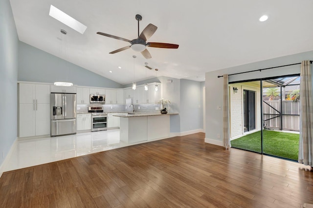 kitchen with open floor plan, a peninsula, stainless steel appliances, light wood-type flooring, and white cabinetry