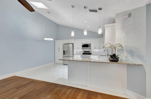 kitchen featuring a skylight, a peninsula, light stone countertops, stainless steel appliances, and a sink