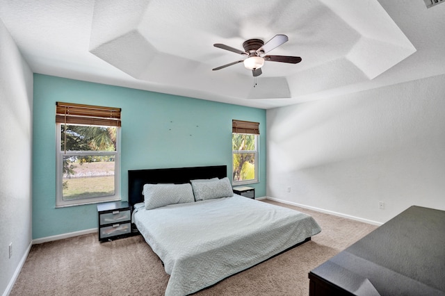 carpeted bedroom featuring a textured ceiling, ceiling fan, visible vents, baseboards, and a raised ceiling