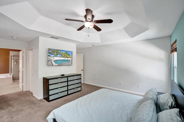 carpeted bedroom with visible vents, baseboards, a ceiling fan, ensuite bath, and a tray ceiling