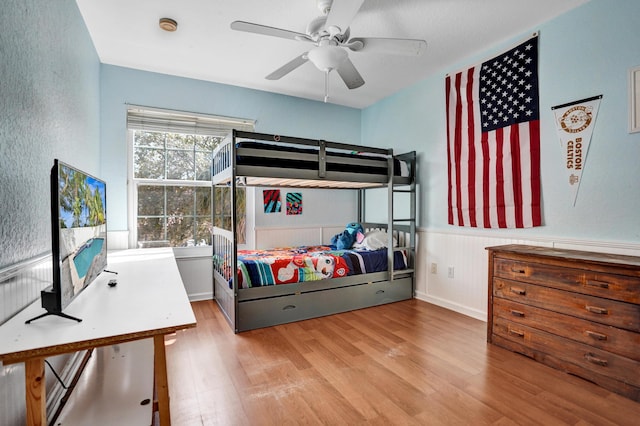 bedroom featuring a ceiling fan, wainscoting, and wood finished floors