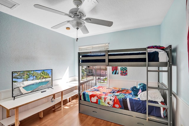 bedroom with a textured ceiling, visible vents, wood finished floors, and a textured wall