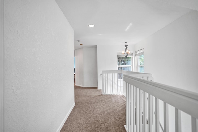 hall featuring carpet floors, an upstairs landing, baseboards, and an inviting chandelier