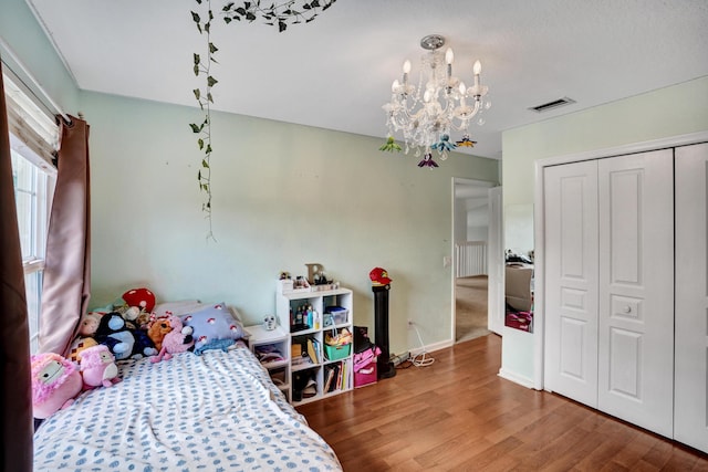 bedroom with a closet, visible vents, an inviting chandelier, wood finished floors, and baseboards